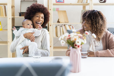 Aunt laughing while holding niece sitting at home