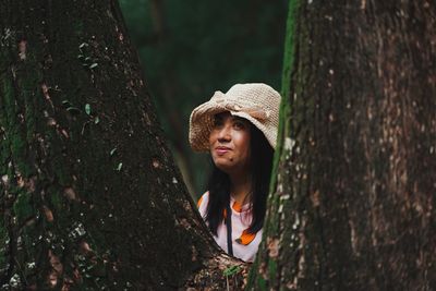 Portrait of beautiful young woman against tree trunk