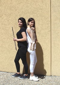 Full length of smiling girls standing against wall