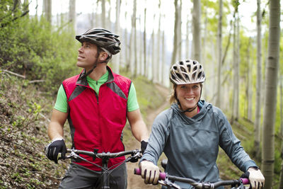 Portrait of female cyclist standing by friend with bicycle in forest