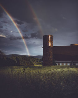 Built structure on field against rainbow in sky