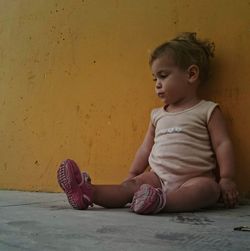 Cute girl sitting on sidewalk against wall