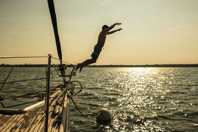 Man surfing in sea against sky during sunset