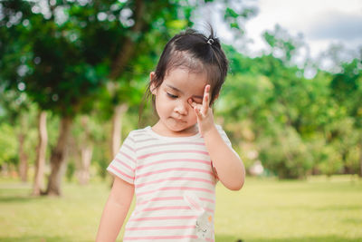 Cute girl rubbing eye while standing on field