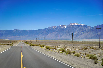 Empty road leading towards mountains against blue sky