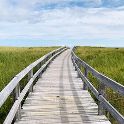 View of wooden footbridge on field against sky