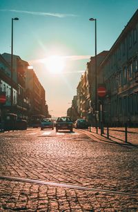 Cars moving on street amidst buildings against sky during sunset