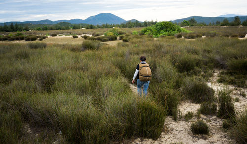 Rear view of woman carrying backpack while walking on grassy field