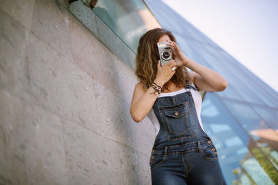 Full length of woman photographing against wall