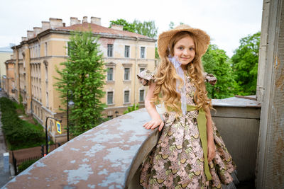 Little girl in dress and hat posing on the balcony