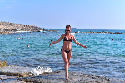 Full length of woman in bikini walking on rock at beach