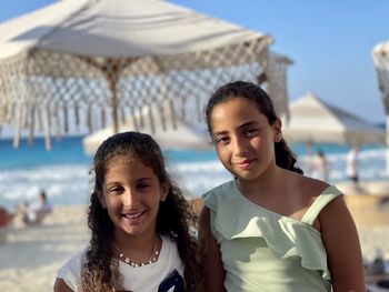 Portrait of two young girls at the beach with umbrella in the background. 