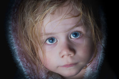 Close-up portrait of cute girl with blue eyes against black background