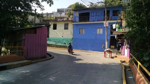 Man on road by house against sky