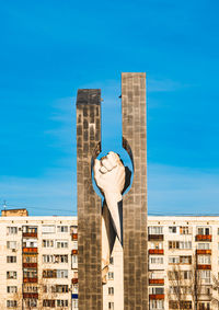 Low angle view of statue by building against blue sky