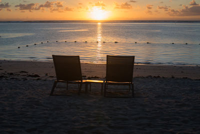 Chair on beach against sky during sunset