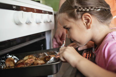 Cooking for family dinner. excited girl, grandmother takes pan with baked roast chicken out of oven