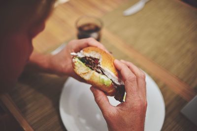 Cropped image of person eating hamburger at table