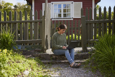 Woman with laptop in front of wooden house