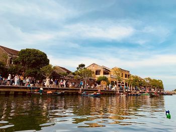 People on lake by buildings against sky