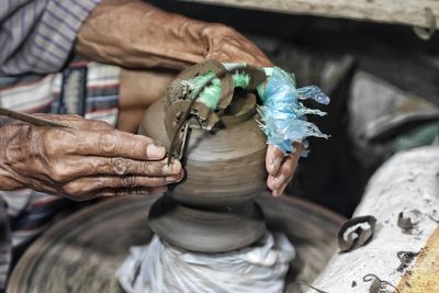 Midsection of man making earthenware on pottery wheel