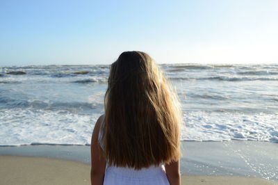 Rear view of woman standing at beach against clear sky