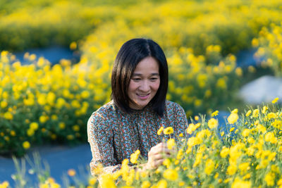 Portrait of smiling young woman with yellow flower in field