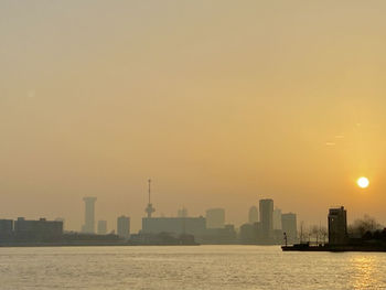 Sea and buildings against sky during sunset