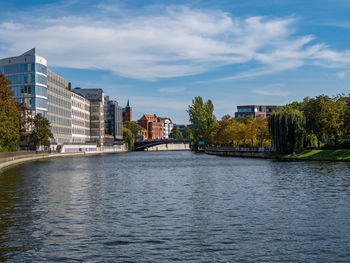 Buildings by river against sky