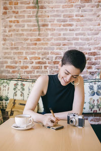 Young woman with short hair writing on note pad in cafe