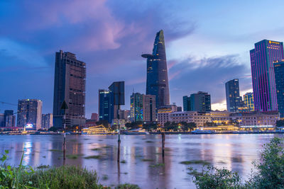 Illuminated modern buildings by bay against sky