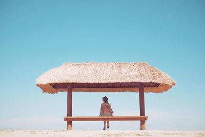 Rear view of woman sitting on roof against clear sky