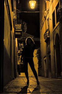 Rear view of woman walking on street amidst buildings at night