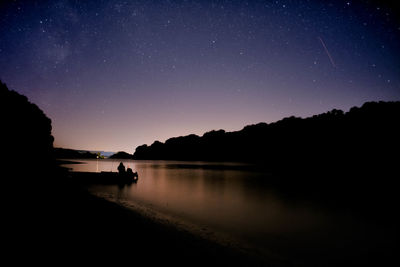 Silhouette people on lake against sky at night