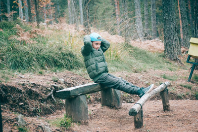 Boy looking away while sitting on seat in forest