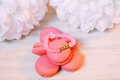 High angle view of pink macaroons with love bracelet on table