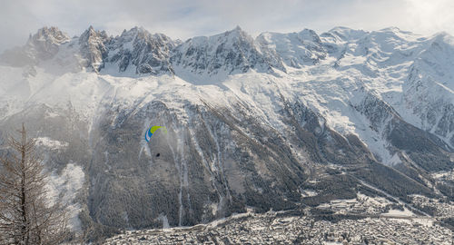 Person paragliding over snow covered mountains against sky