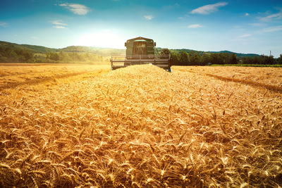 Tractor on grassy field against sky during sunny day