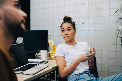 Young businesswoman looking away while sitting in meeting with colleagues at creative office