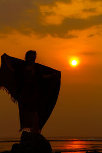 Side view of woman standing against sea during sunset