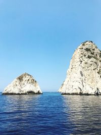 Rocks in sea against clear blue sky