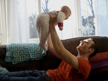 Father lifting baby girl while lying on sofa