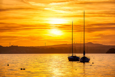 Silhouette sailboat on sea against romantic sky at sunset