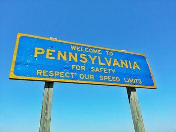 Close-up of welcome to pennsylvania signboard against blue sky