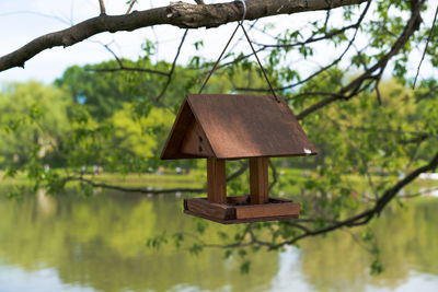 Wooden birdhouse hanging on branch against lake
