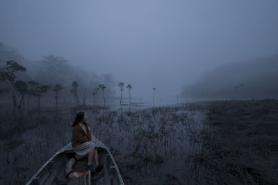 Woman sitting in boat on lake during foggy weather