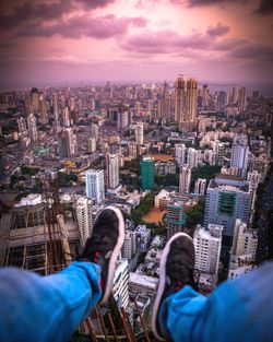 Low section of person sitting above cityscape at sunset