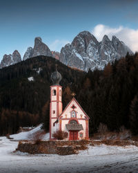 House on snowcapped mountains against sky during winter