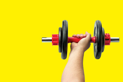 Close-up of hand holding colored pencils against yellow background