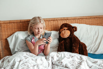 Cute girl sitting in bed in morning and texting talking at social media on smartphone cellphone. 